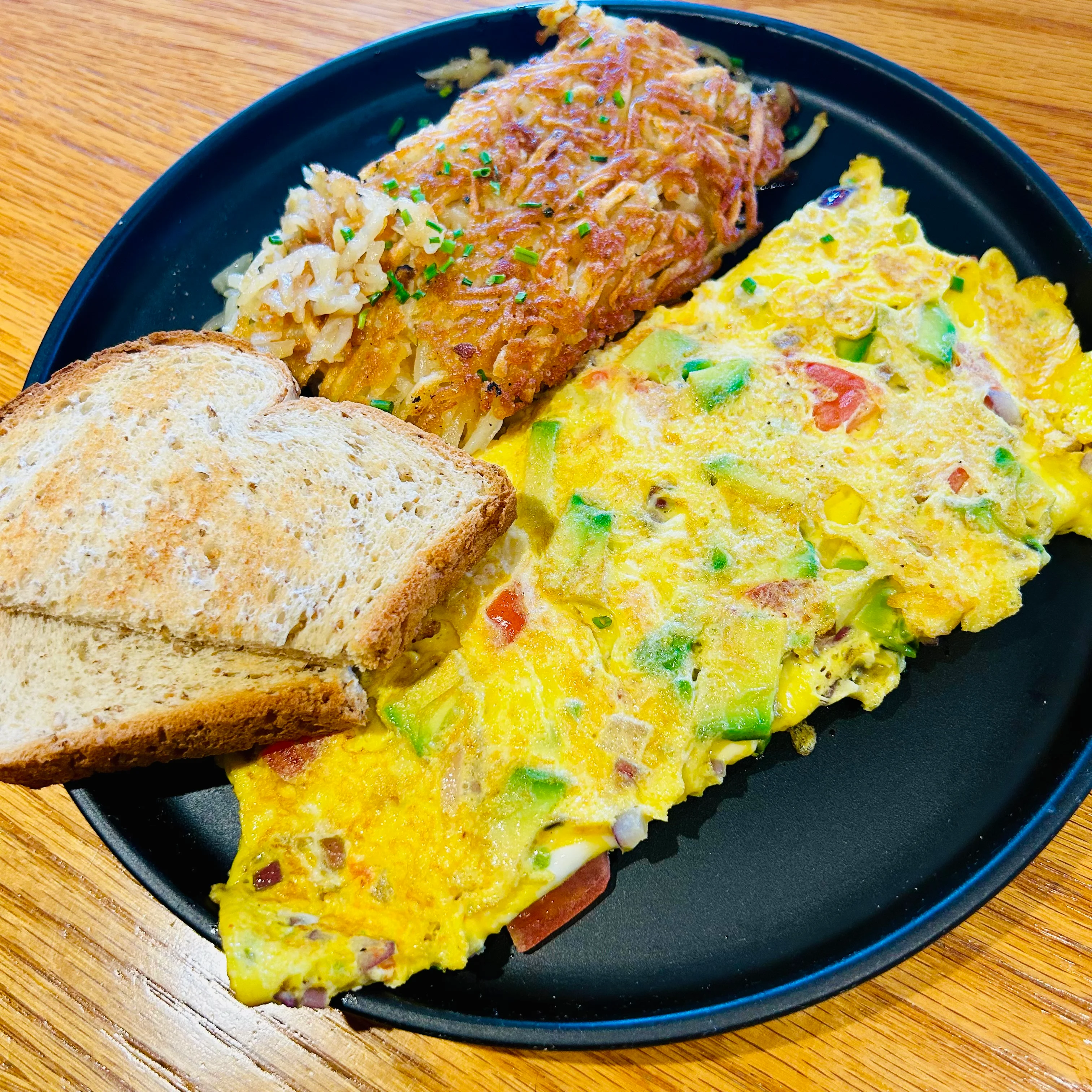 A hearty breakfast plate featuring a vegetable omelette, crispy hashbrowns, and toasted bread.