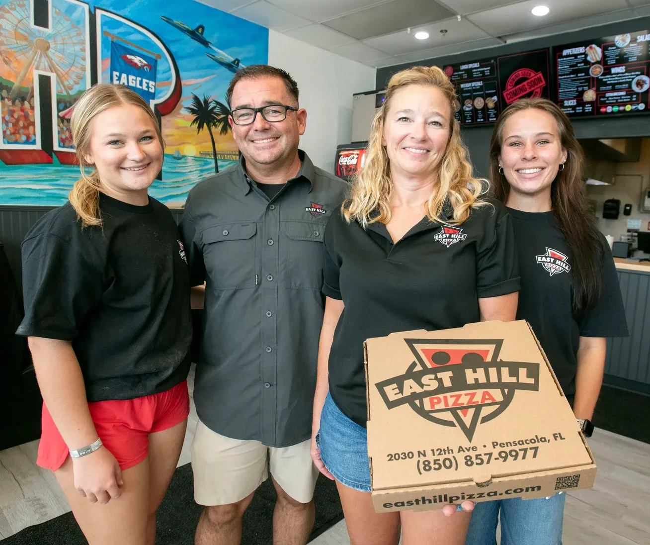 Smiling pizza restaurant team holding a branded box inside the restaurant
