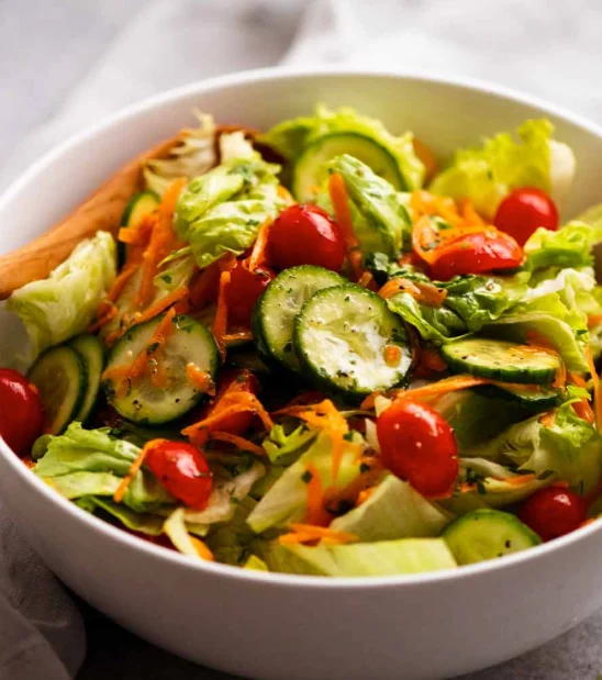A fresh garden salad featuring a mix of lettuce, cucumber slices, grape tomatoes, and carrots, served in a large bowl.