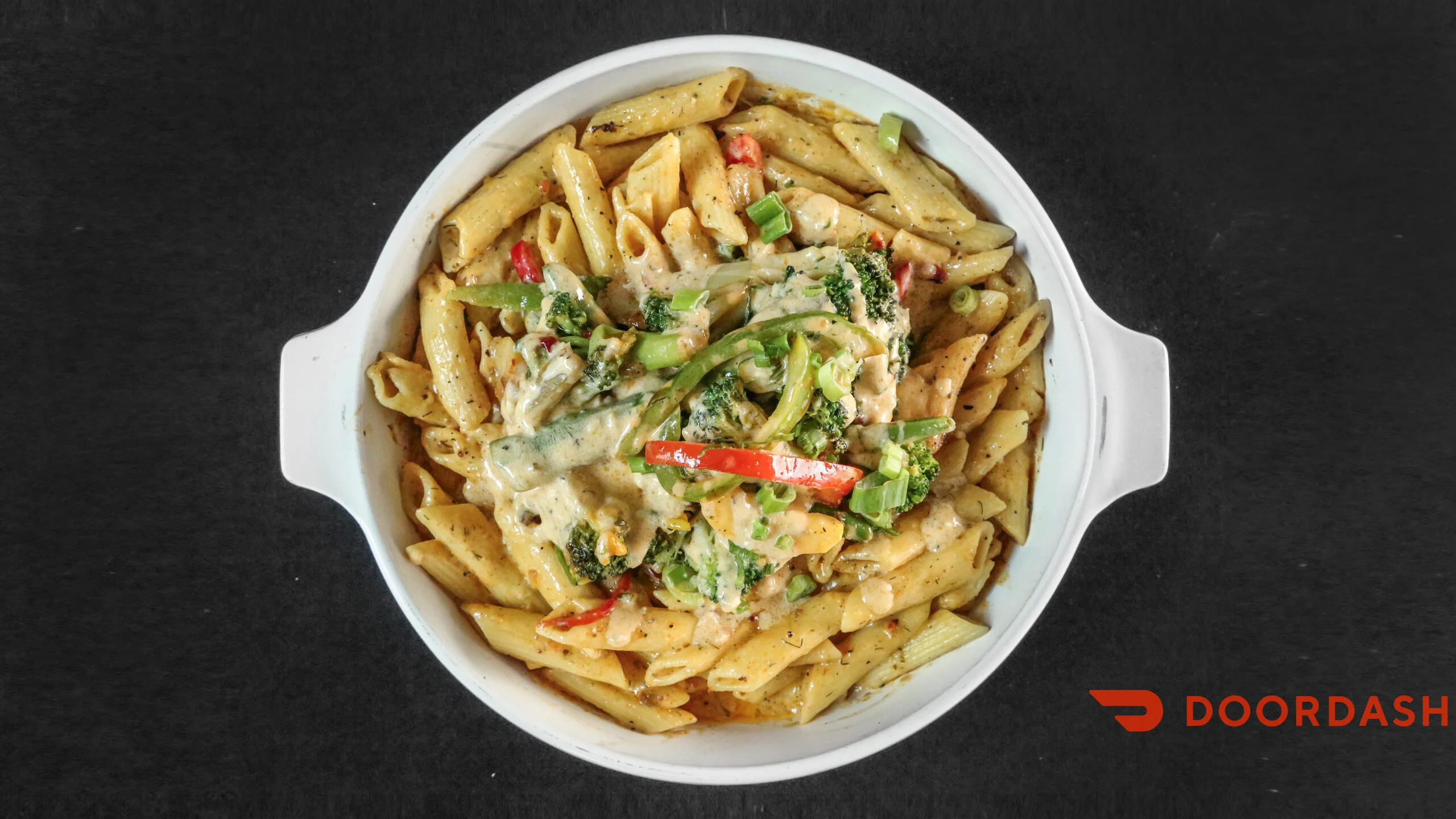 A creamy pasta dish with penne noodles, mixed vegetables, and sauce in a white bowl.
