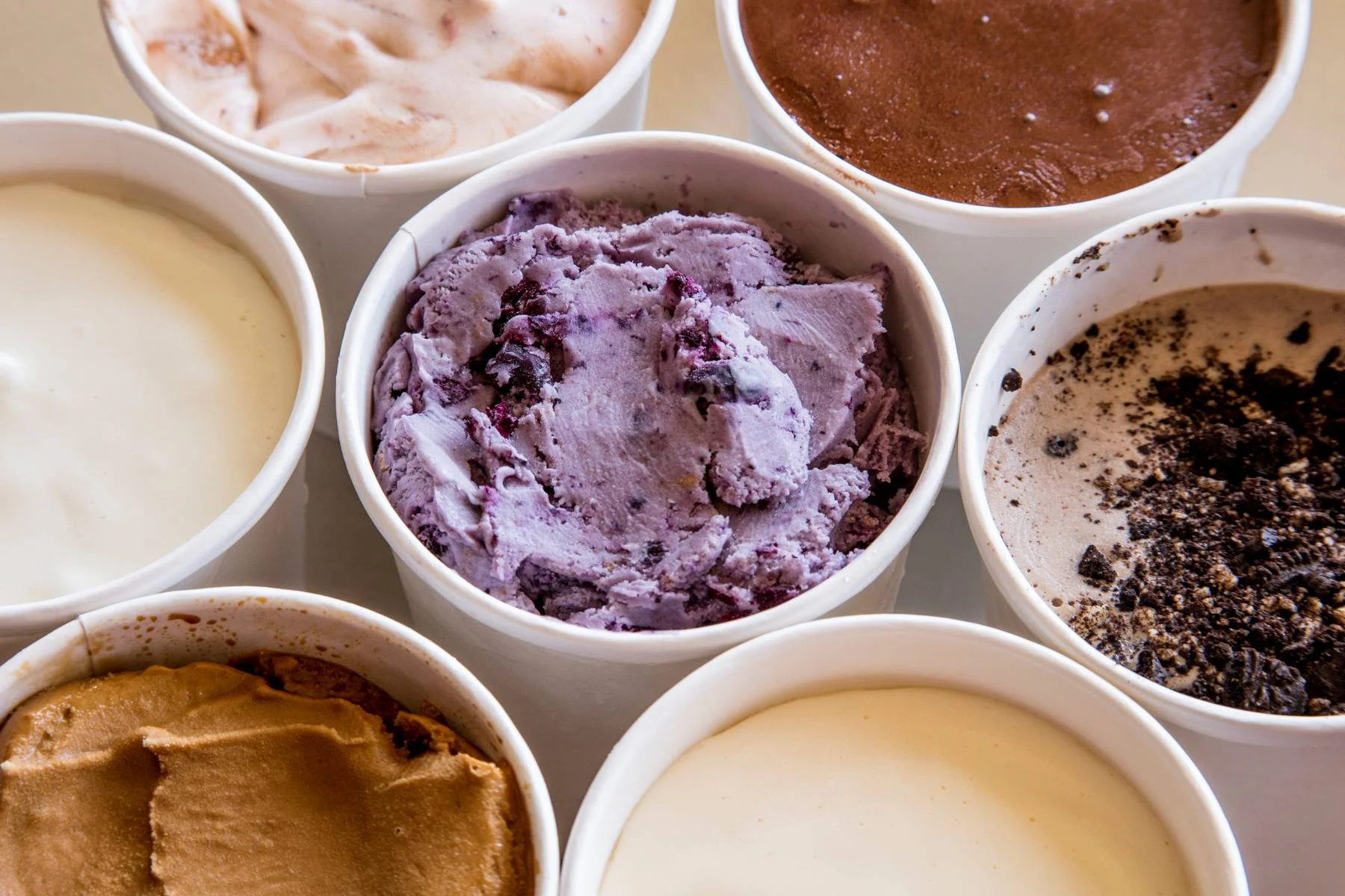 Assorted gourmet ice cream flavors in white cups, including blueberry, chocolate, cookies and cream, caramel, and vanilla, from a local artisanal ice cream shop