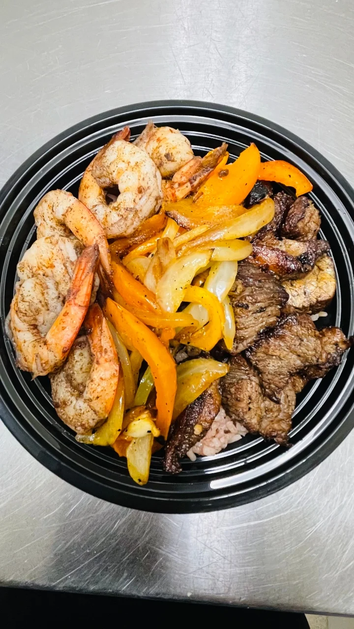 A delicious meal featuring grilled shrimp and beef, accompanied by sautéed bell peppers and onions, all served in a black plate.