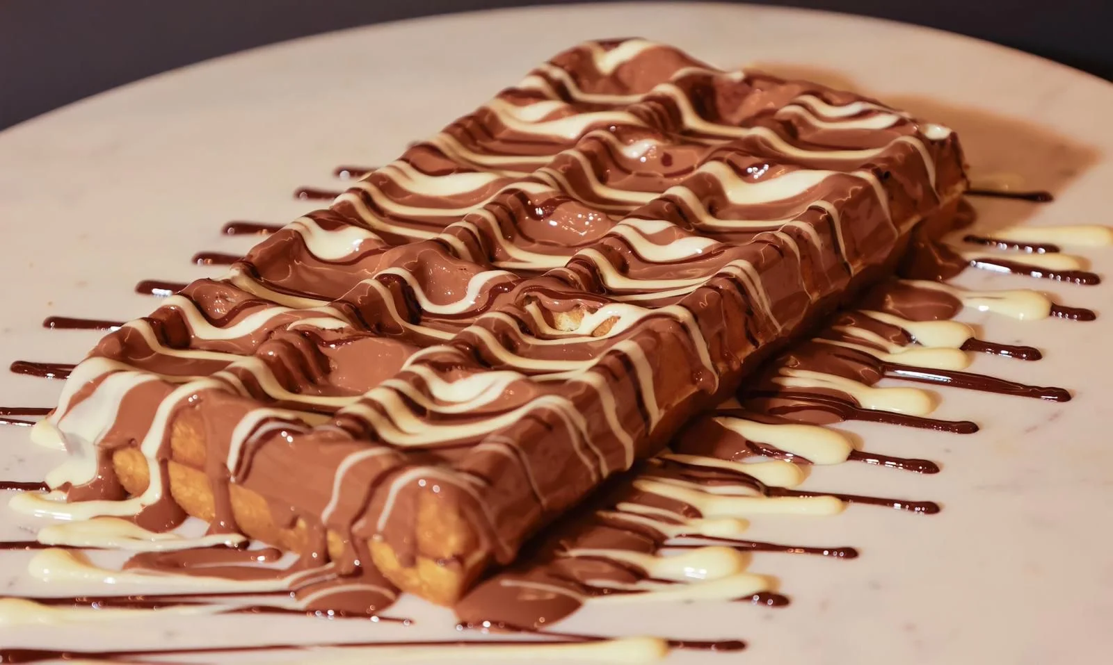 A simple yet elegant chocolate dish, featuring a layered chocolate base with a glossy chocolate and white drizzle, served on a white plate.