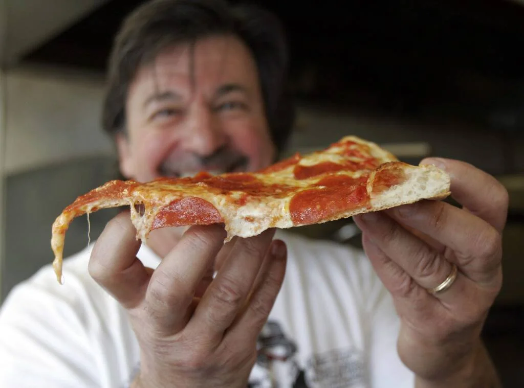 Pepperoni pizza slice held by a smiling chef