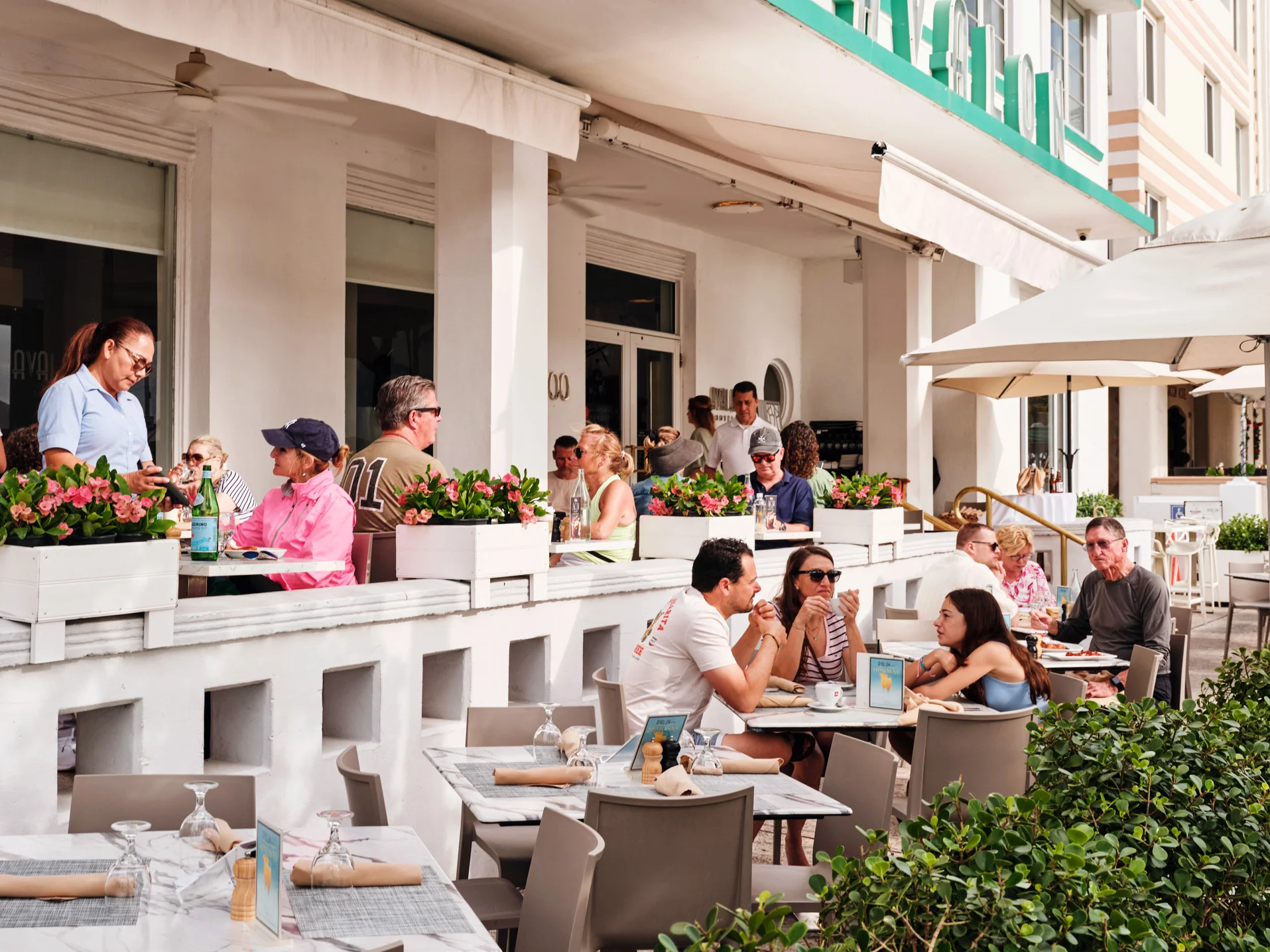 A vibrant Art Deco building with palm trees and an American flag, featuring an outdoor dining area.