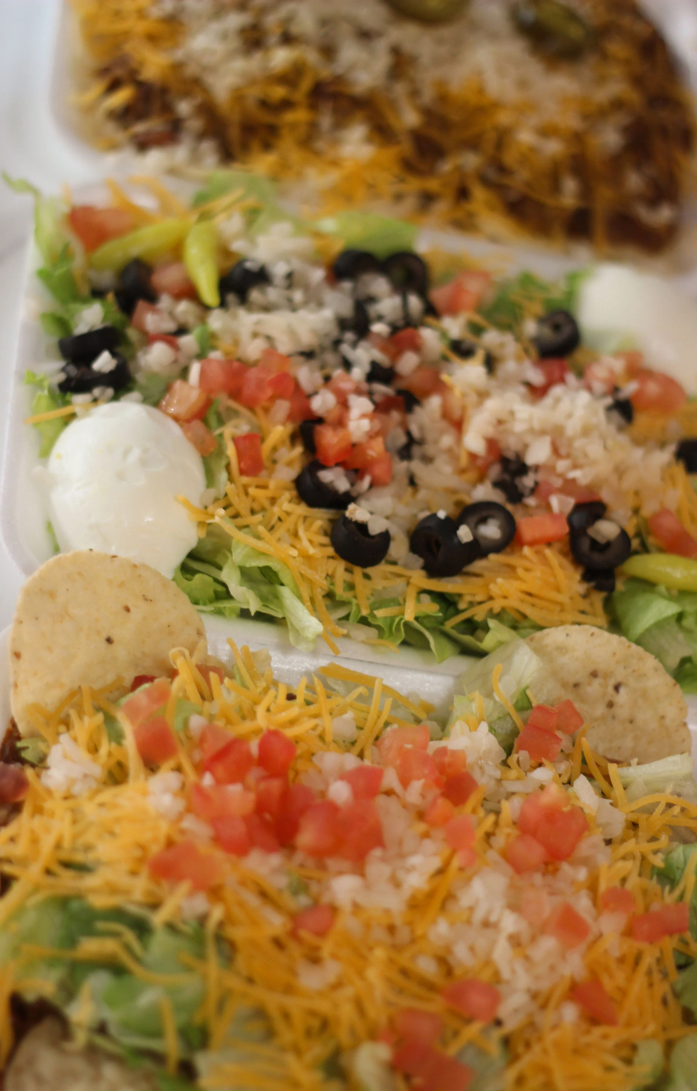 An assortment of tacos and a salad with toppings like lettuce, tomatoes, olives, and shredded cheese on a white tray.