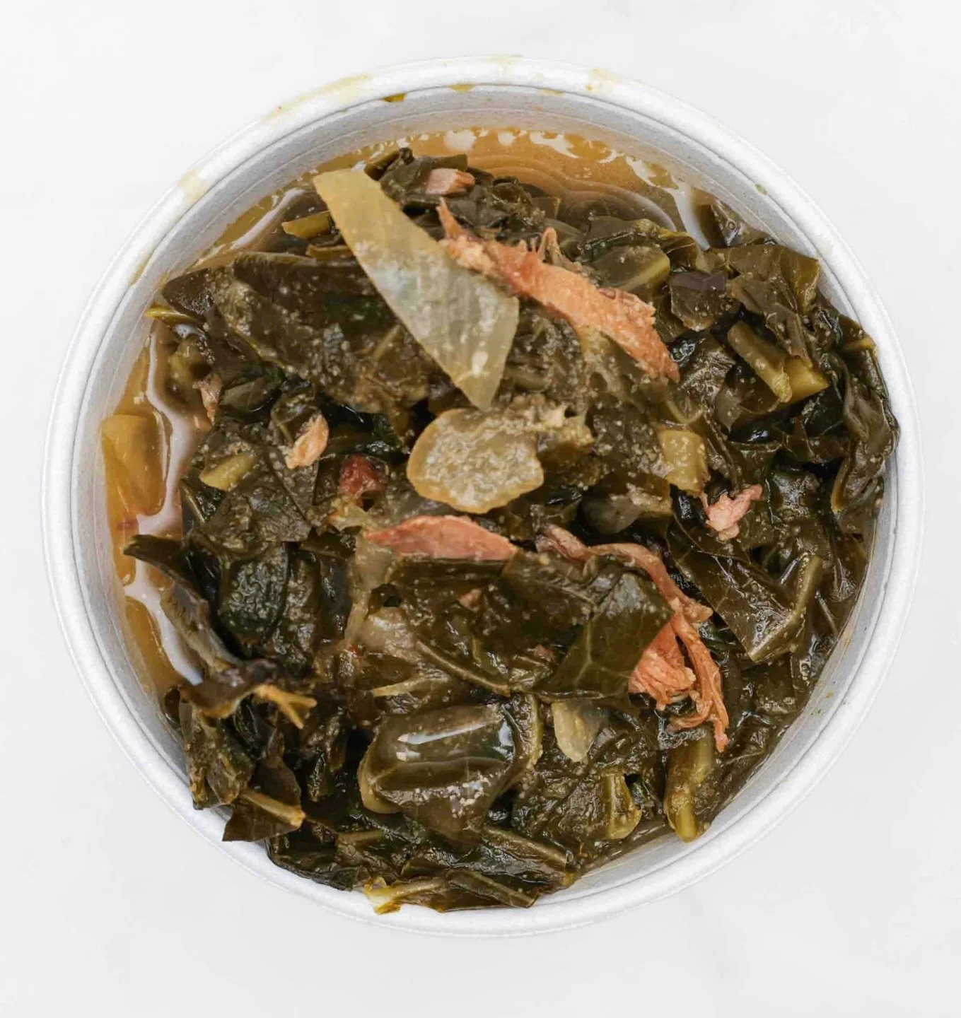 A bowl of cooked collard greens with pieces of meat and spices in a savory broth.