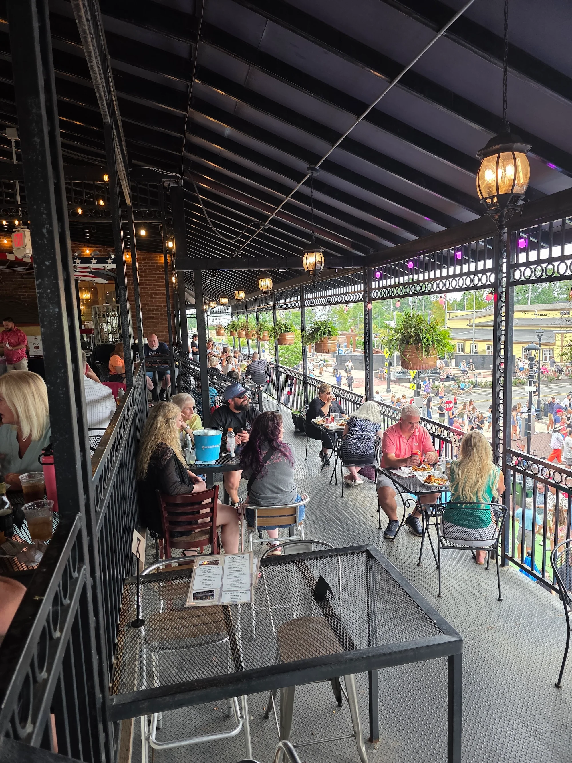 A lively outdoor dining venue with people sitting at tables on a balcony, enjoying their meals and drinks.