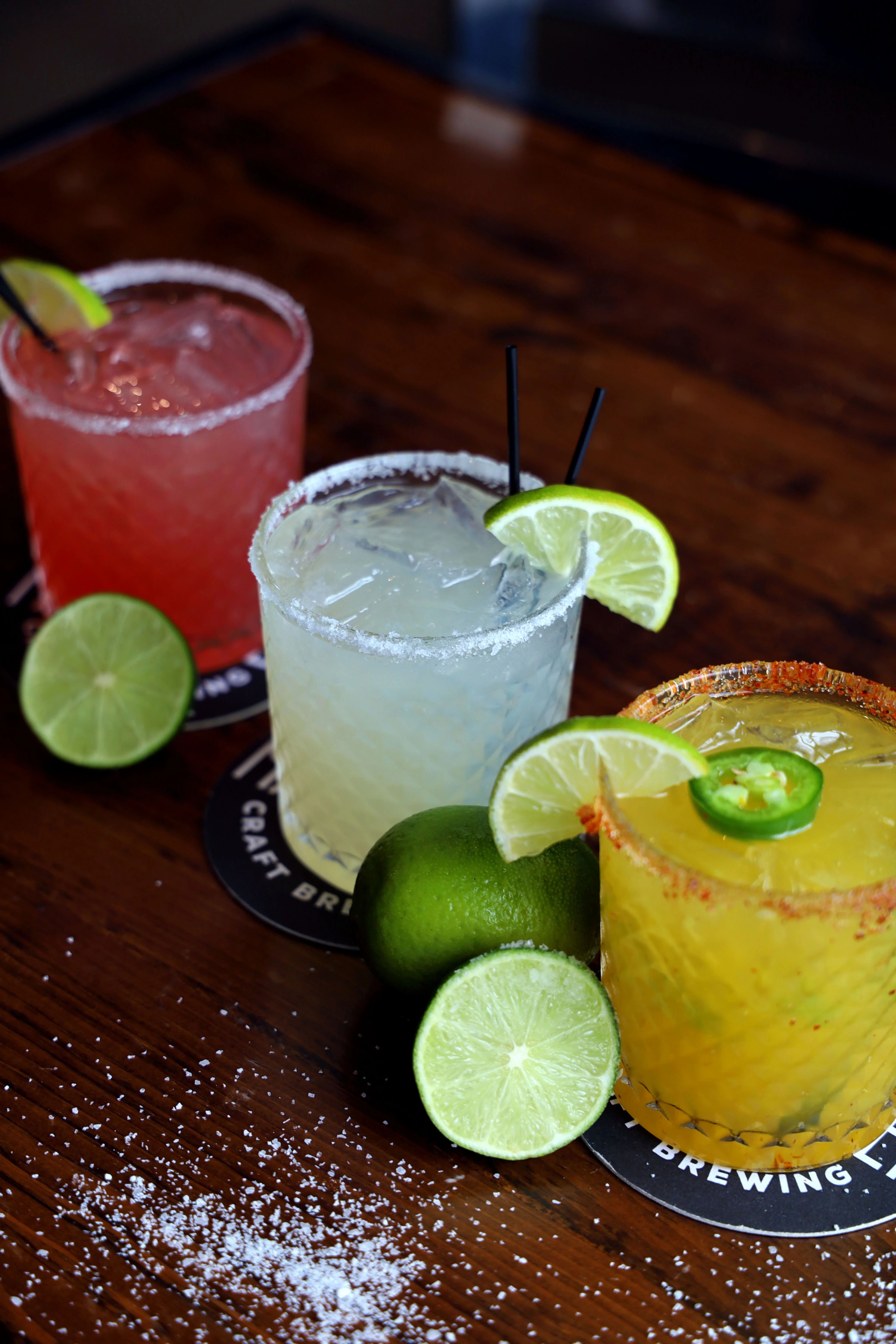 Three colorful cocktails on a table, showcasing vibrant garnishes.