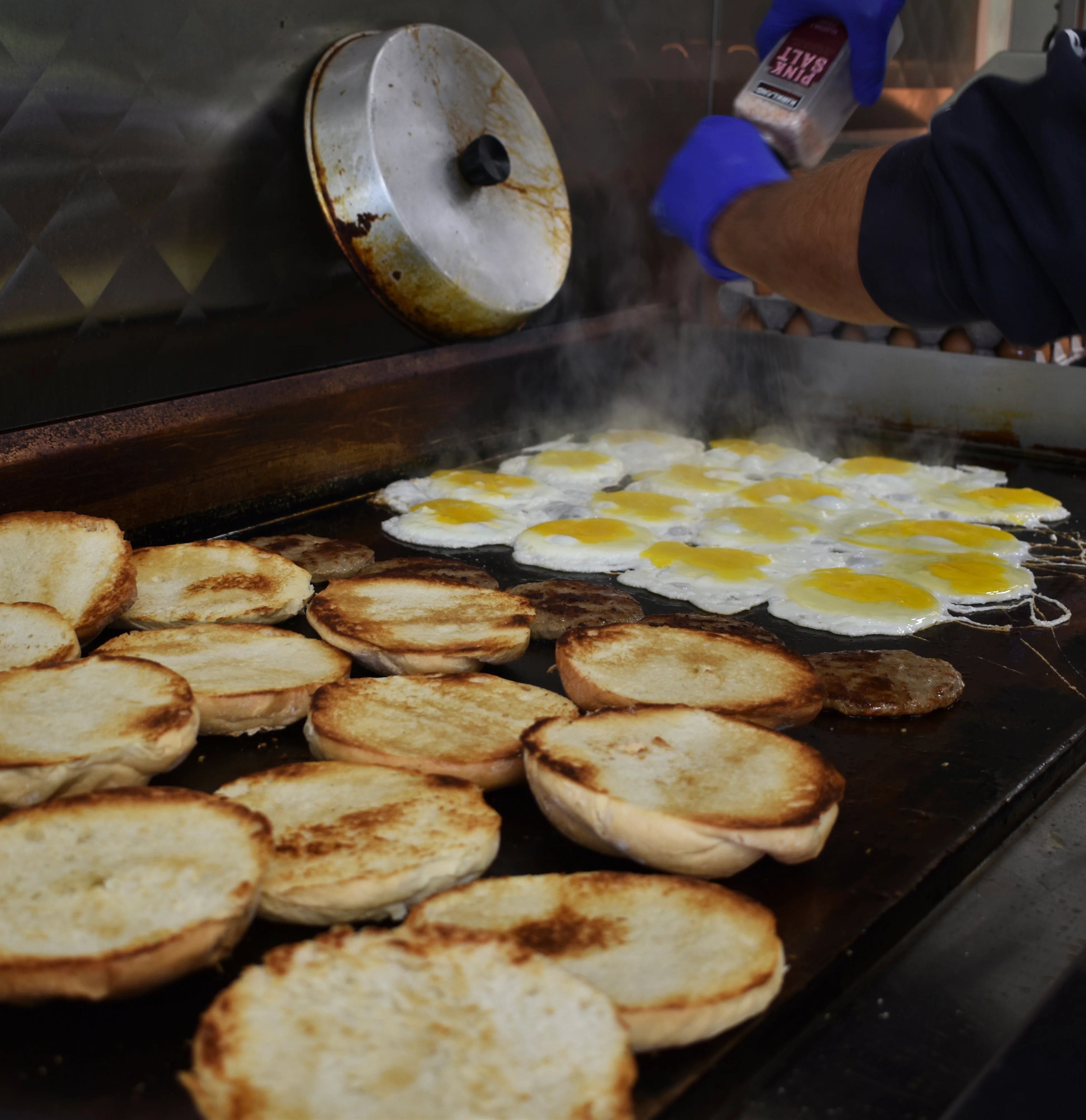 Fried eggs and toasted buns on a griddle for breakfast sandwiches