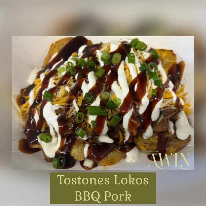 A dish featuring tostones topped with BBQ pork, cheese, green onions, sour cream, and a barbecue sauce, served in a container.