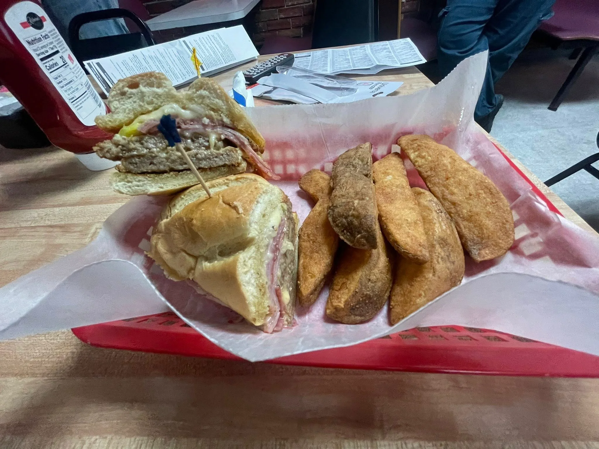 A plate featuring a sandwich with layers of meat, cheese, and vegetables, accompanied by golden potato wedges.