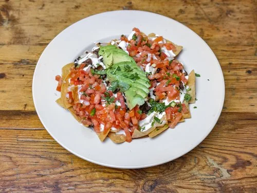 Plate of Mexican nachos topped with fresh salsa and avocado