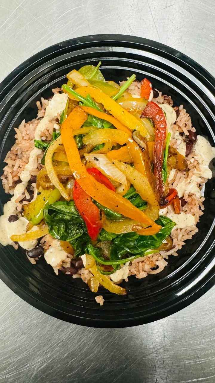 A colorful plate featuring rice, black beans, and a medley of sautéed bell peppers and spinach, garnished with a creamy dressing.