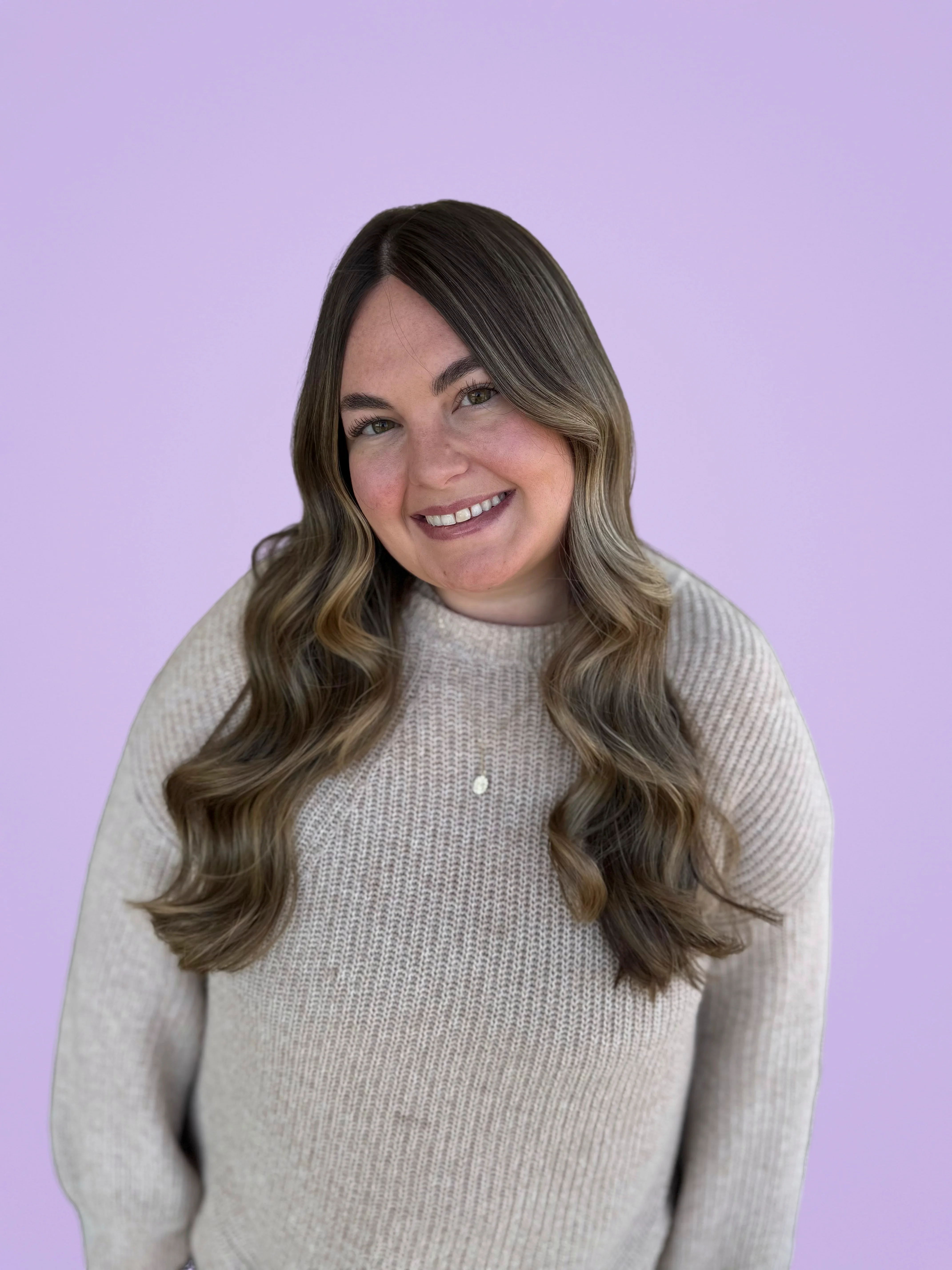 Smiling woman with long hair in a cozy sweater against a purple background