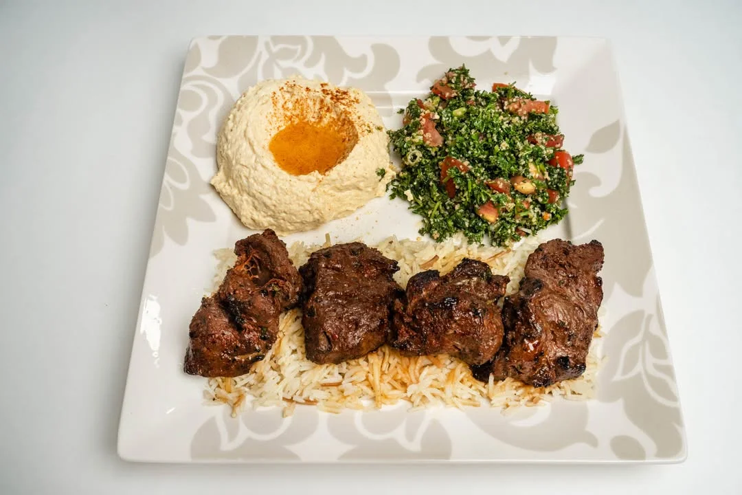 A plate featuring grilled meat served over rice, accompanied by hummus and a fresh tabbouleh salad.