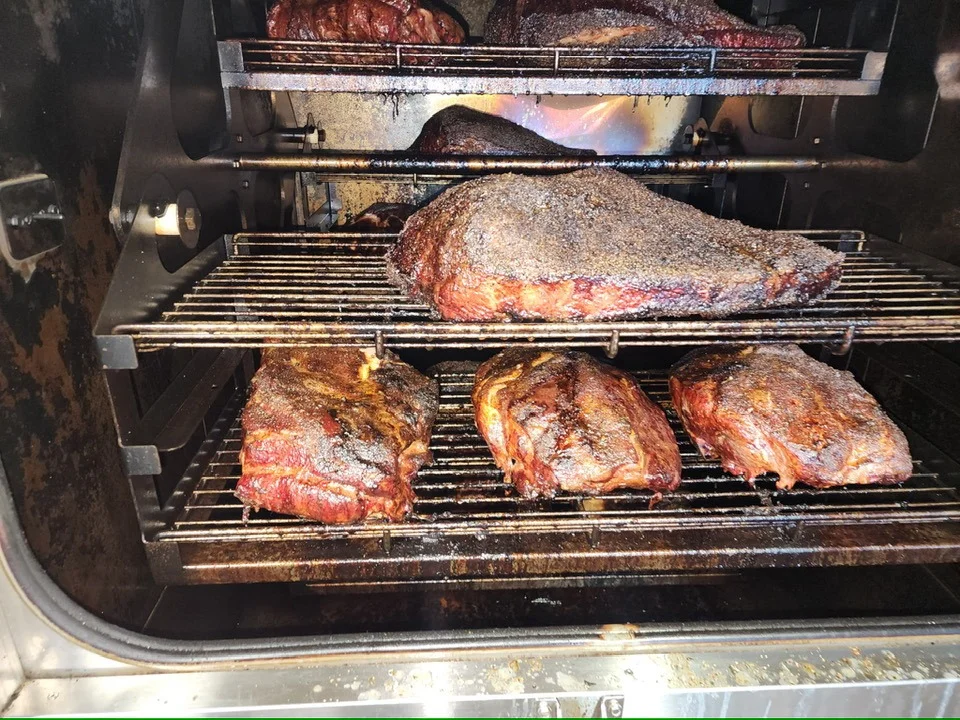 An inside view of a smoker filled with various cuts of smoked meat, showcasing a rich, dark crust.