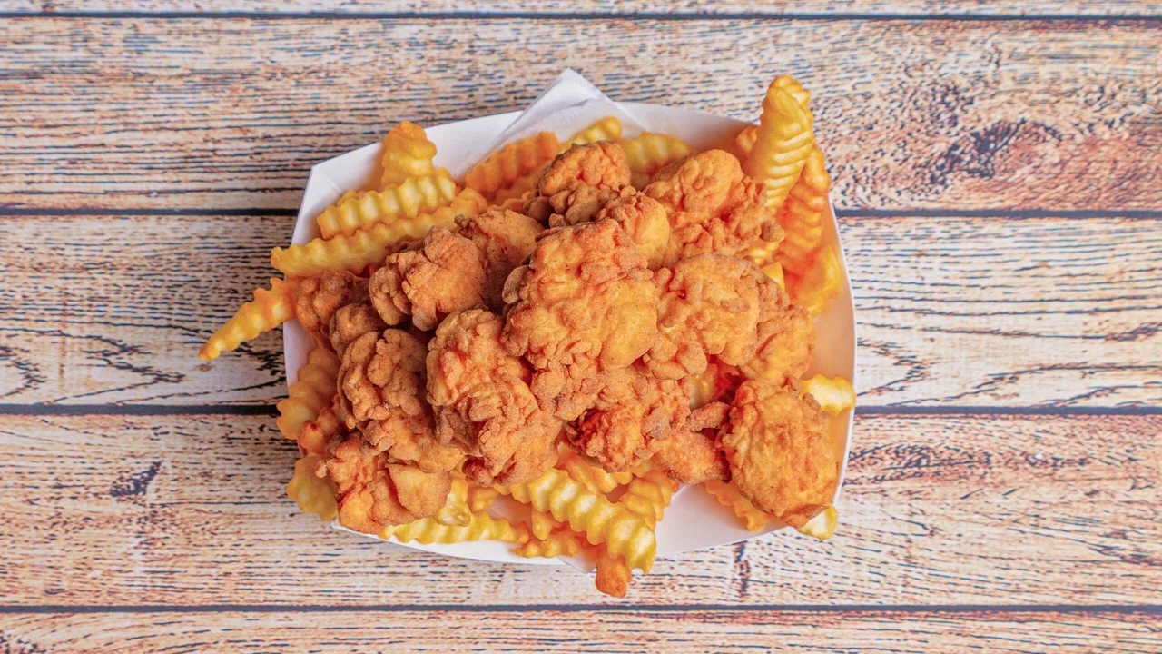 A serving of fried chicken pieces placed on a bed of crinkle-cut fries, served in a white tray.