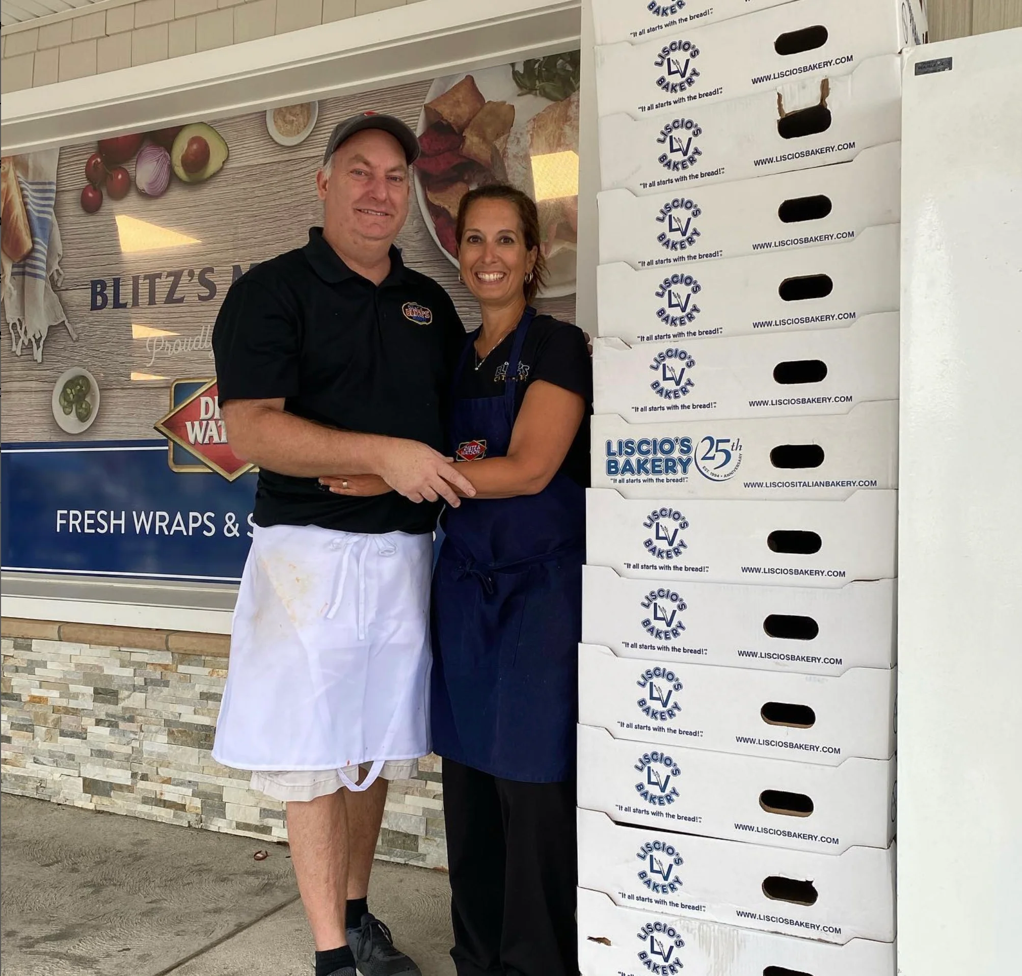 Restaurant owners posing with stacked bakery boxes