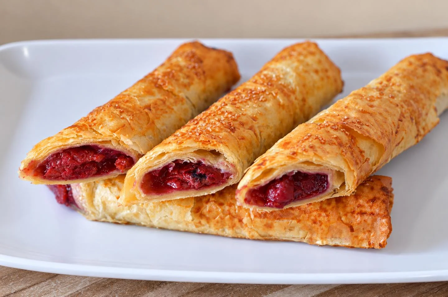 A plate holding three pastry rolls, golden-brown and filled with berry filling.