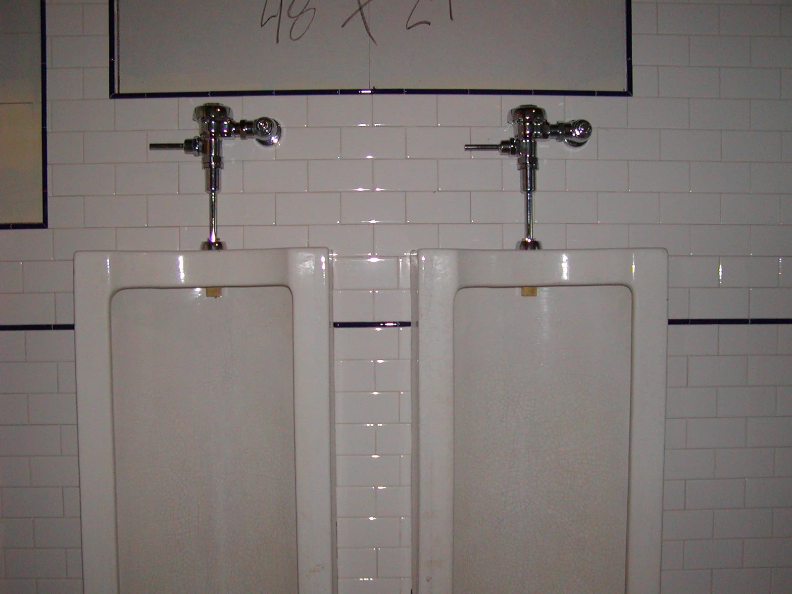 Men's restroom with two white urinals against tiled wall