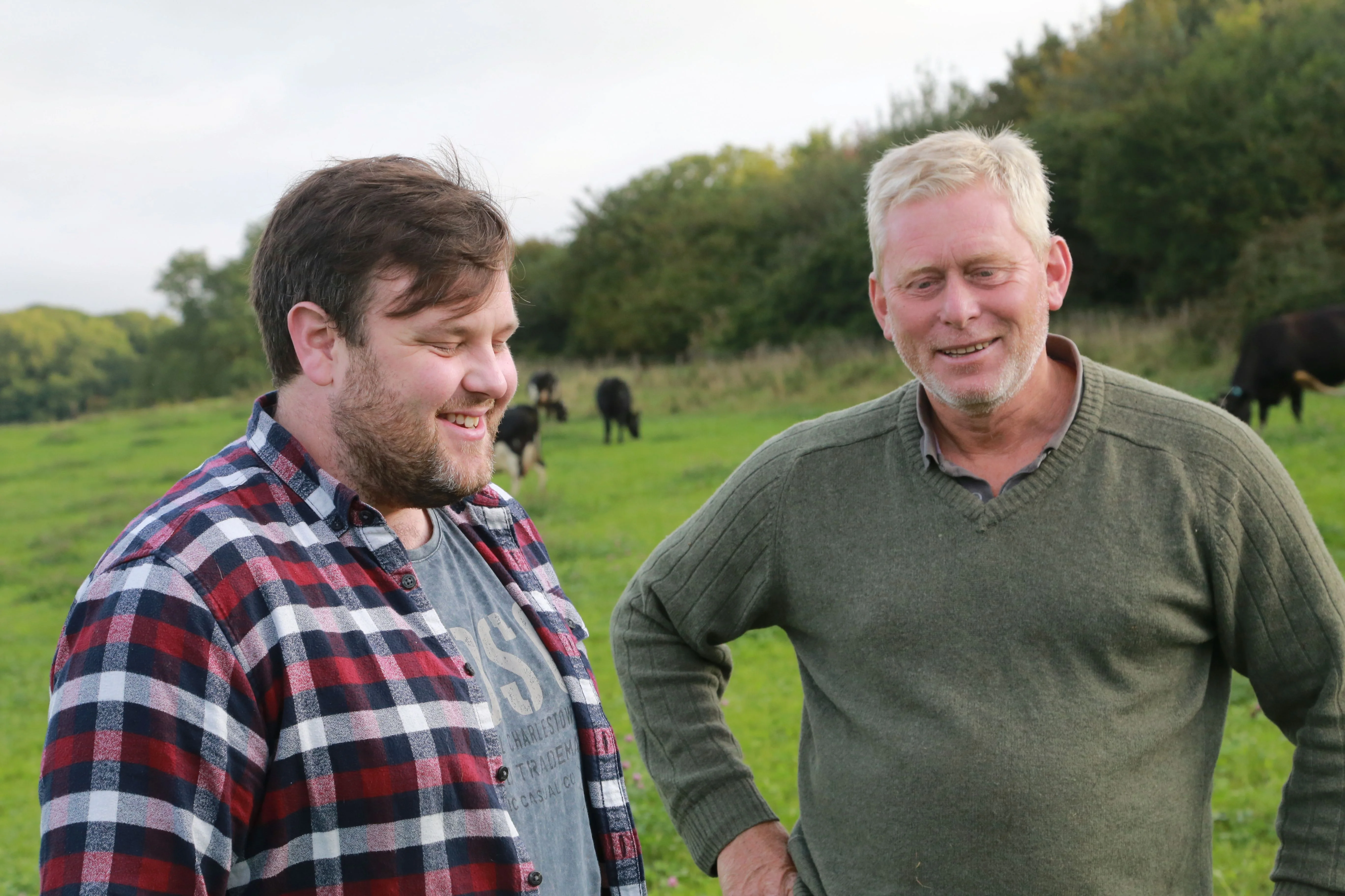 Two farmers smiling in a green pasture with grazing cows