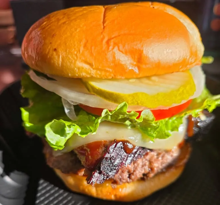 A close-up of a delicious hamburger with lettuce, tomato, pickles, and a slice of cheese, served in a soft bun.