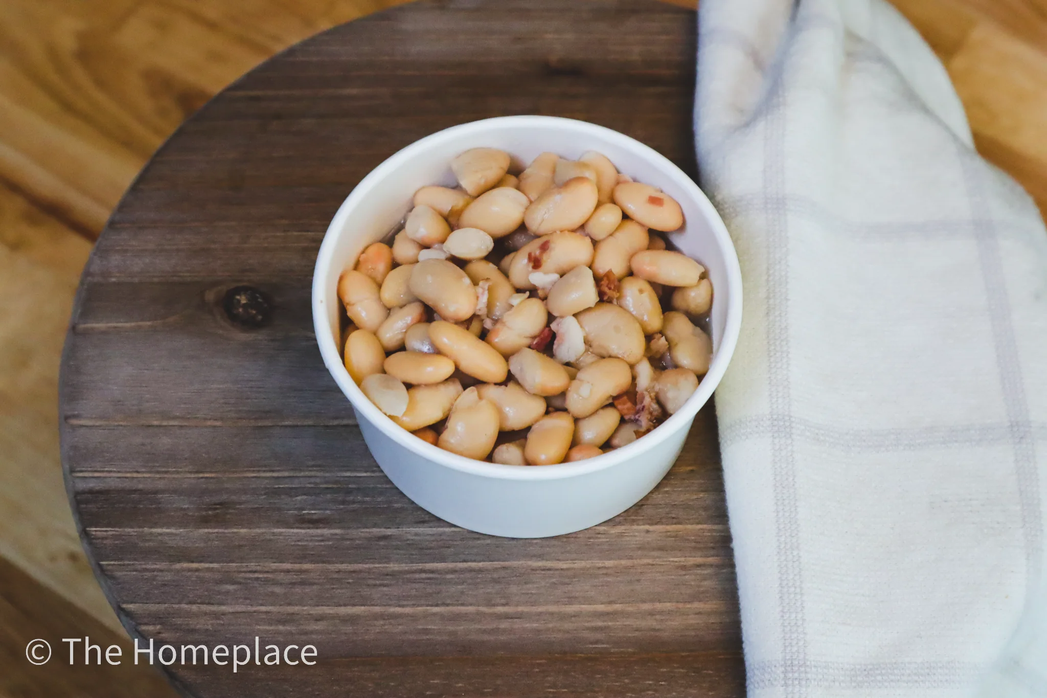 A bowl filled with cooked white beans, showcasing their soft texture, accompanied by a kitchen towel.