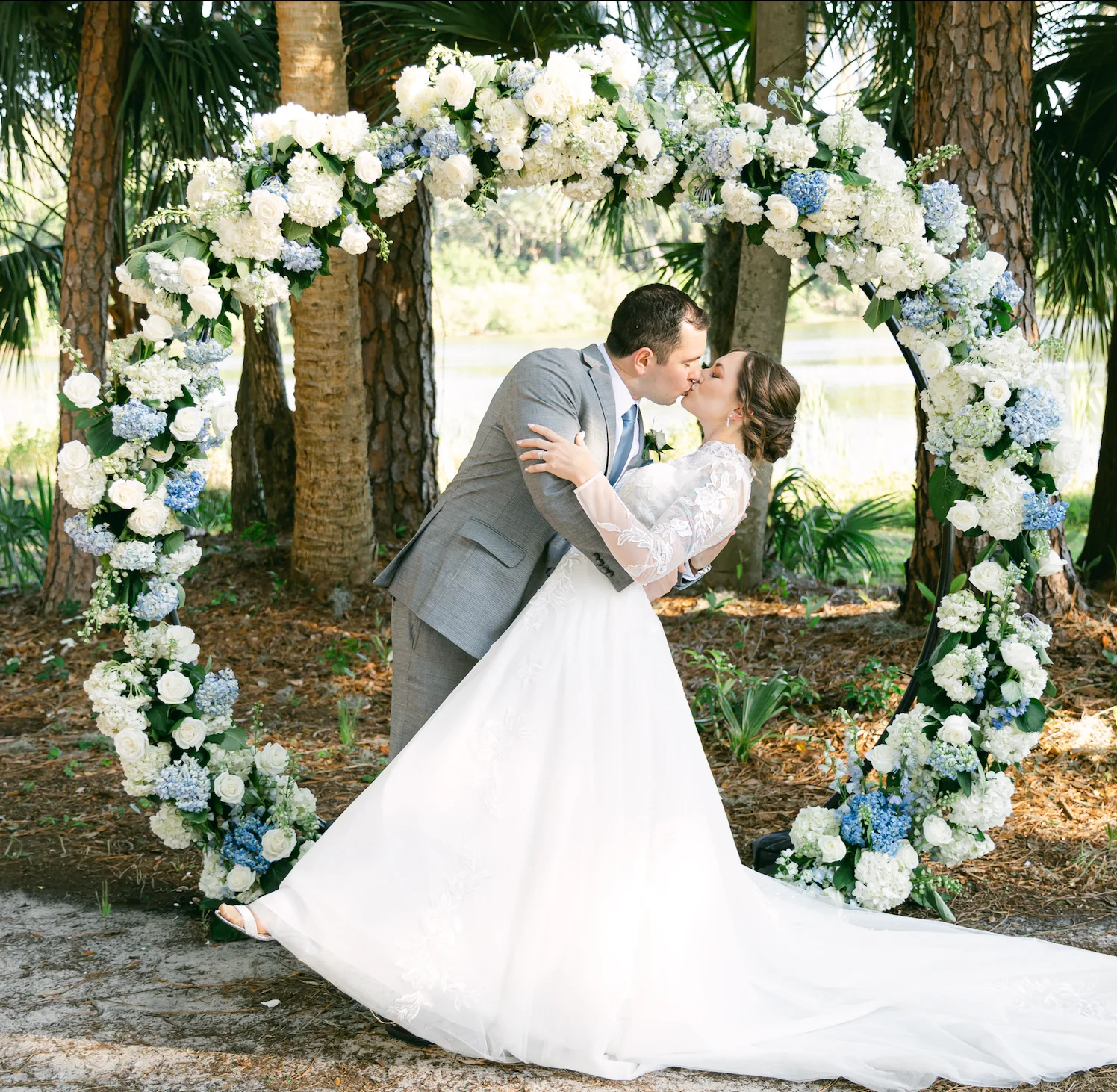 Bride and groom kissing under floral arch at outdoor wedding