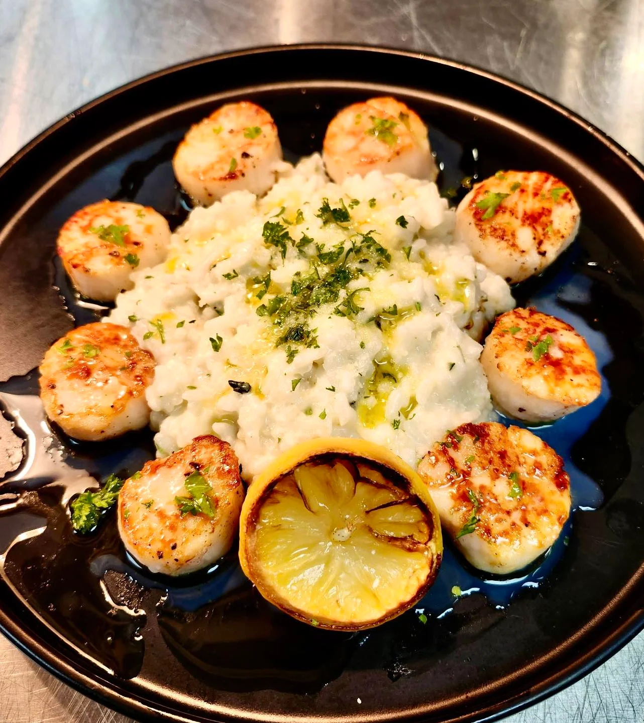 Plate of scallops with risotto and grilled lemon, garnished with herbs.