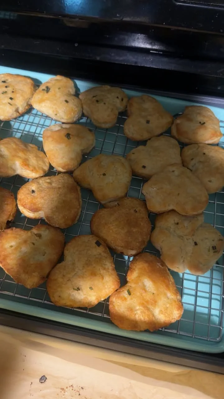 Freshly baked heart-shaped biscuits cooling on a rack. Some are adorned with small herbs.