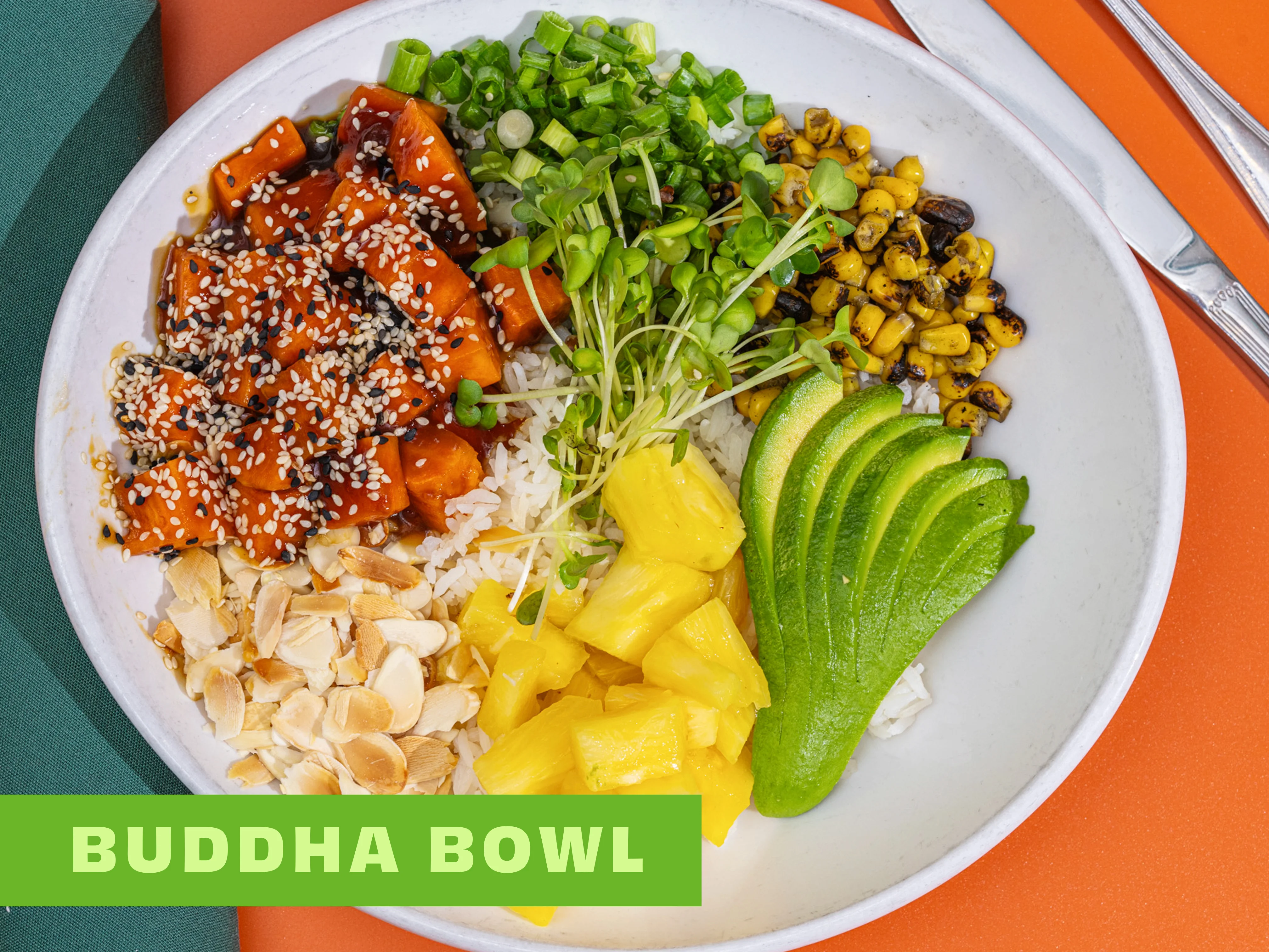 A colorful Buddha bowl featuring rice topped with sauced sweet potatoes, sesame seeds, greens, corn, avocado slices, pineapple chunks, and sliced almonds.