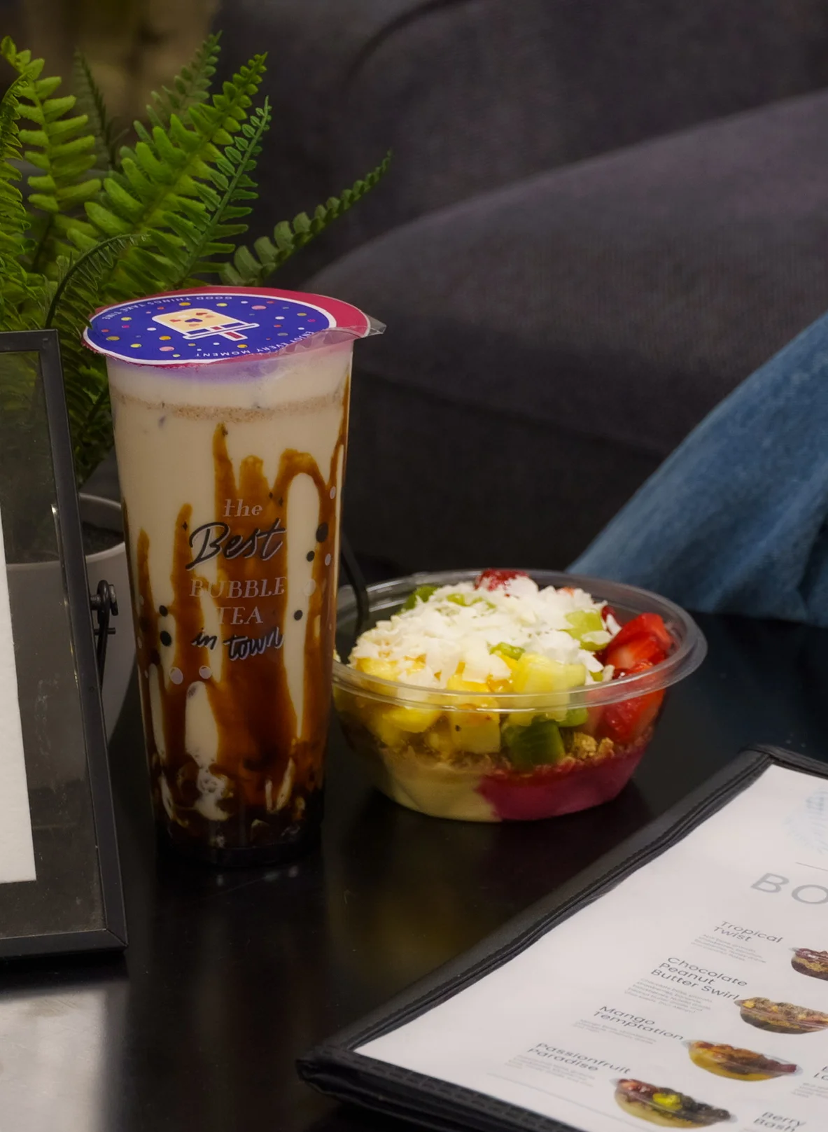 Bubble tea and a colorful fruit bowl on a table with a menu.