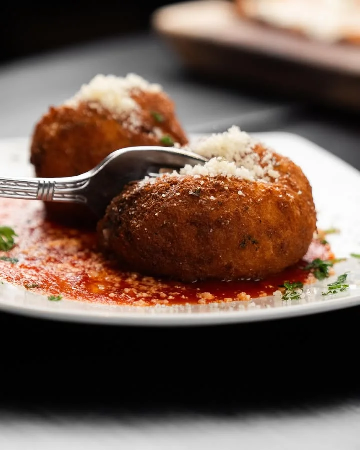 Two crispy fried balls on a plate, garnished with grated cheese and served with a flavorful sauce.