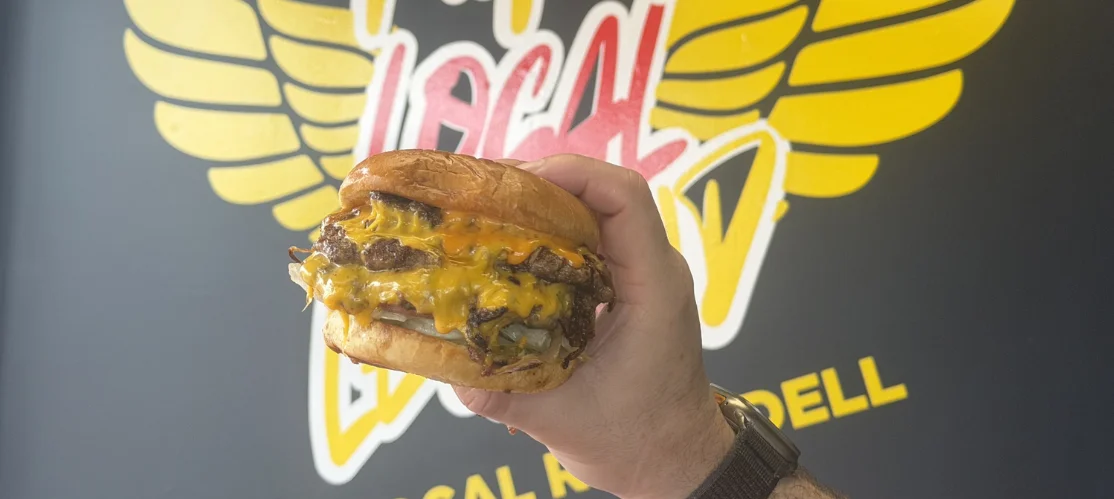 Delicious double onion smash burger with toppings on a wooden table.