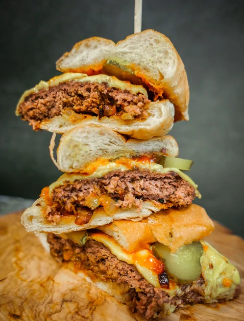 A towering burger made up of multiple patties, cheese, and pickles, layered with sauce between fluffy buns.