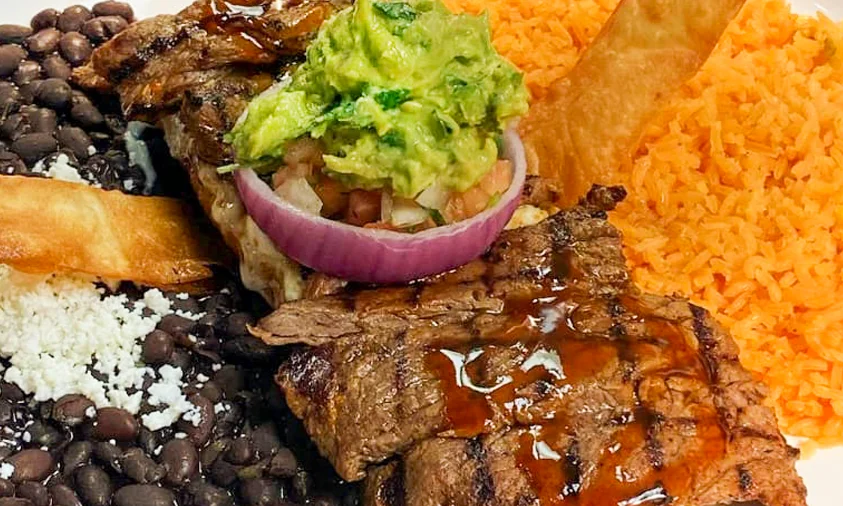 A vibrant display of various Mexican dishes including tacos, nachos, guacamole, and more, all set on a wooden table with a restaurant logo in the center.