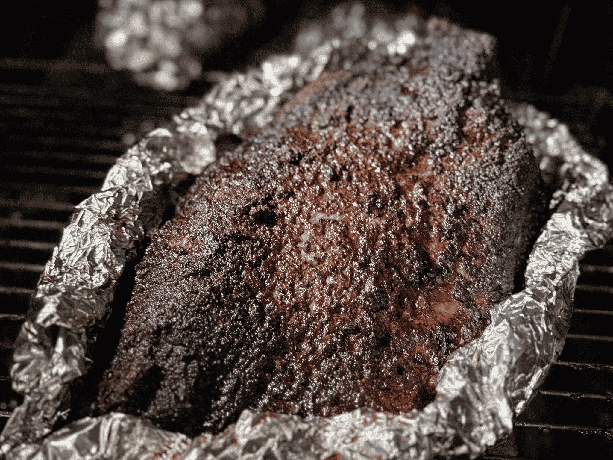 Smoked brisket wrapped in foil, resting on a grill.