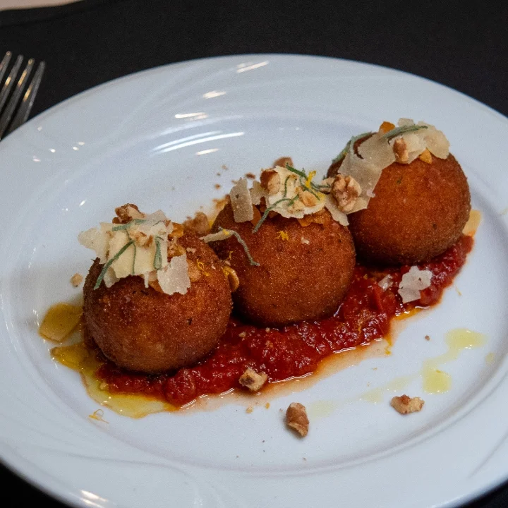 Three crispy balls served on a bed of rich tomato sauce, topped with cheese and nuts for added flavor and texture.