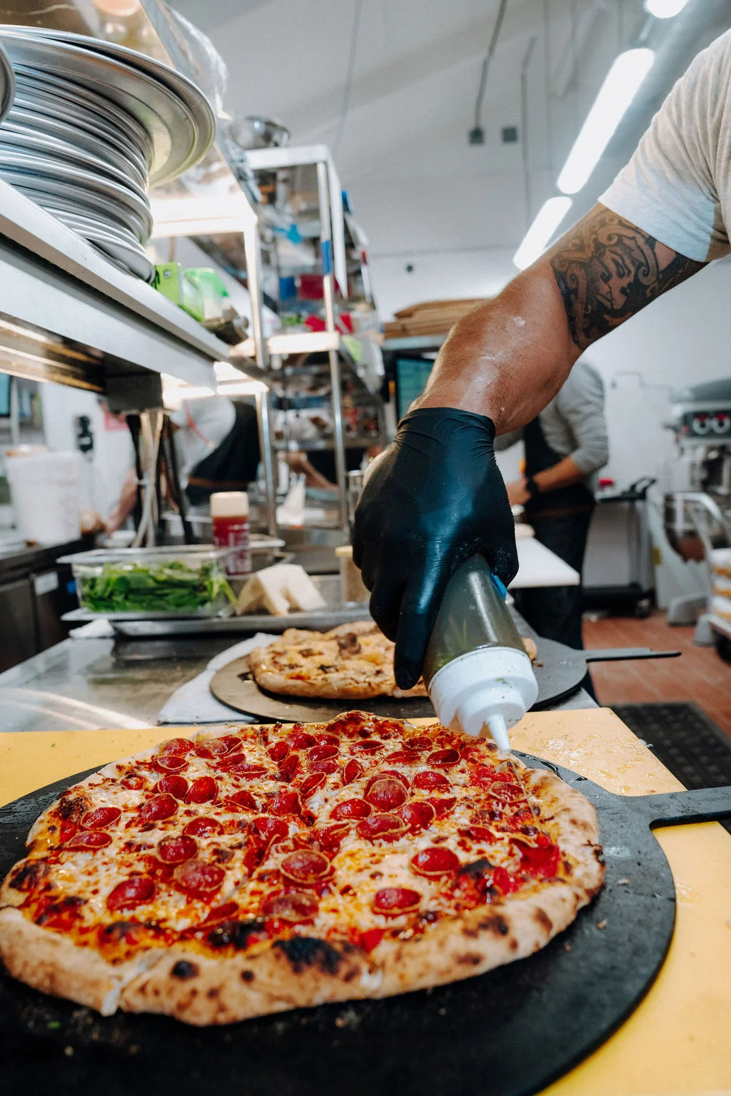 Pepperoni pizza being garnished in a bustling kitchen