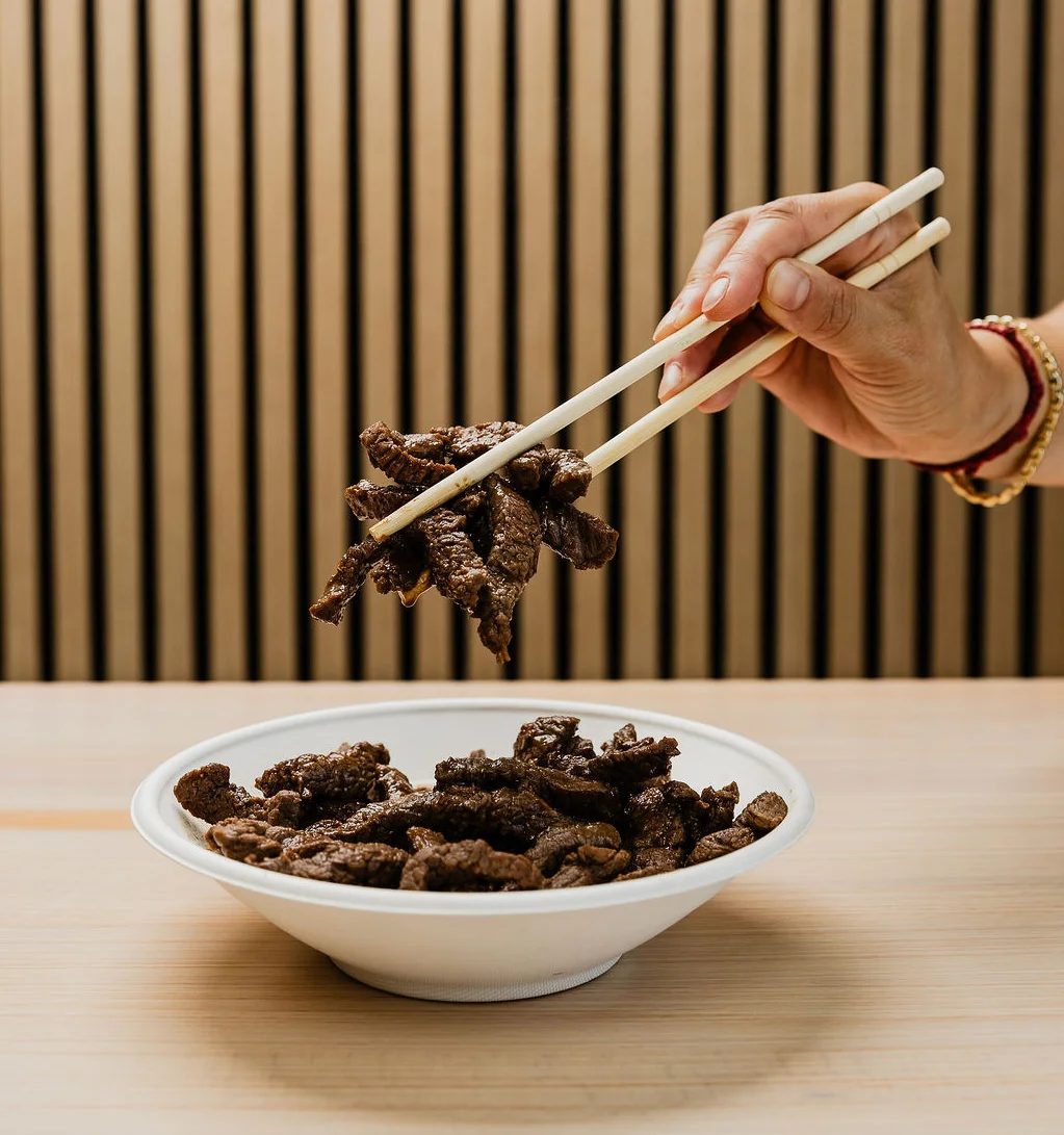 a hand holding up bulgogi steak strips with chopsticks 
