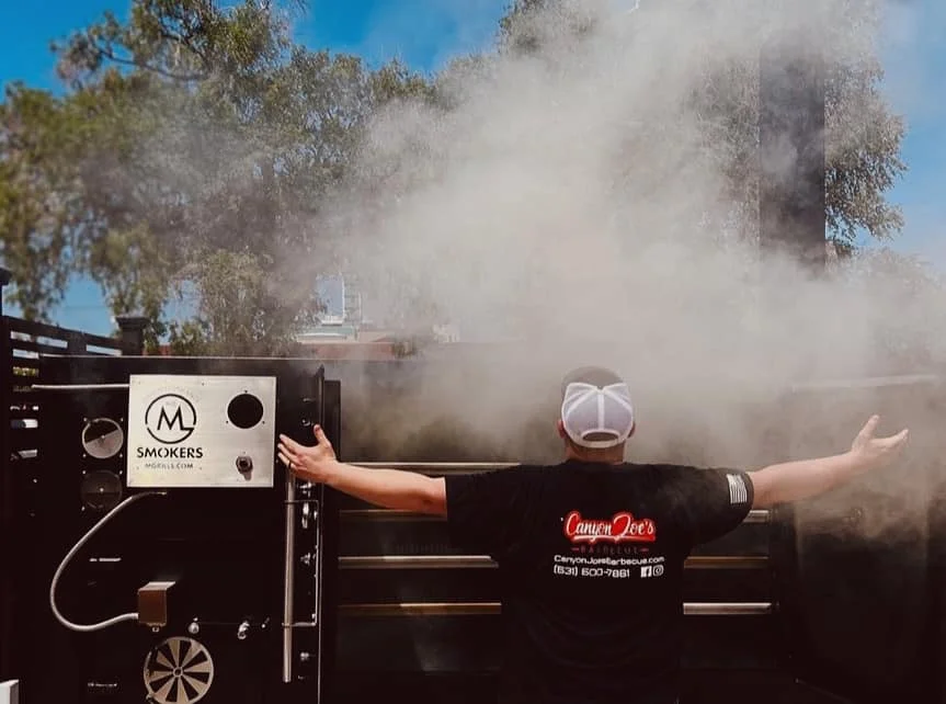 Pitmaster tending to a smoker with billowing smoke