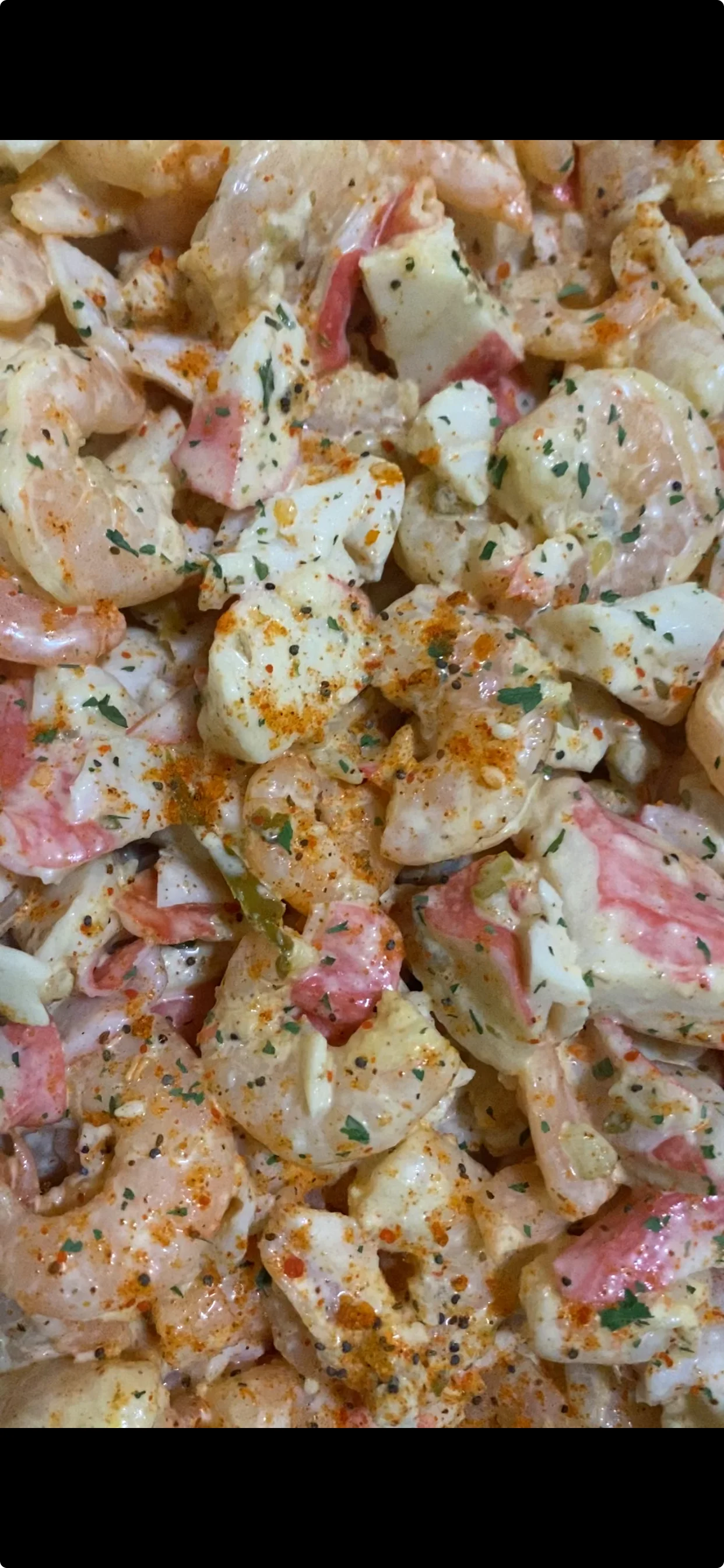 A close-up of a seafood salad featuring shrimp and crab meat, garnished with seasoning and herbs.
