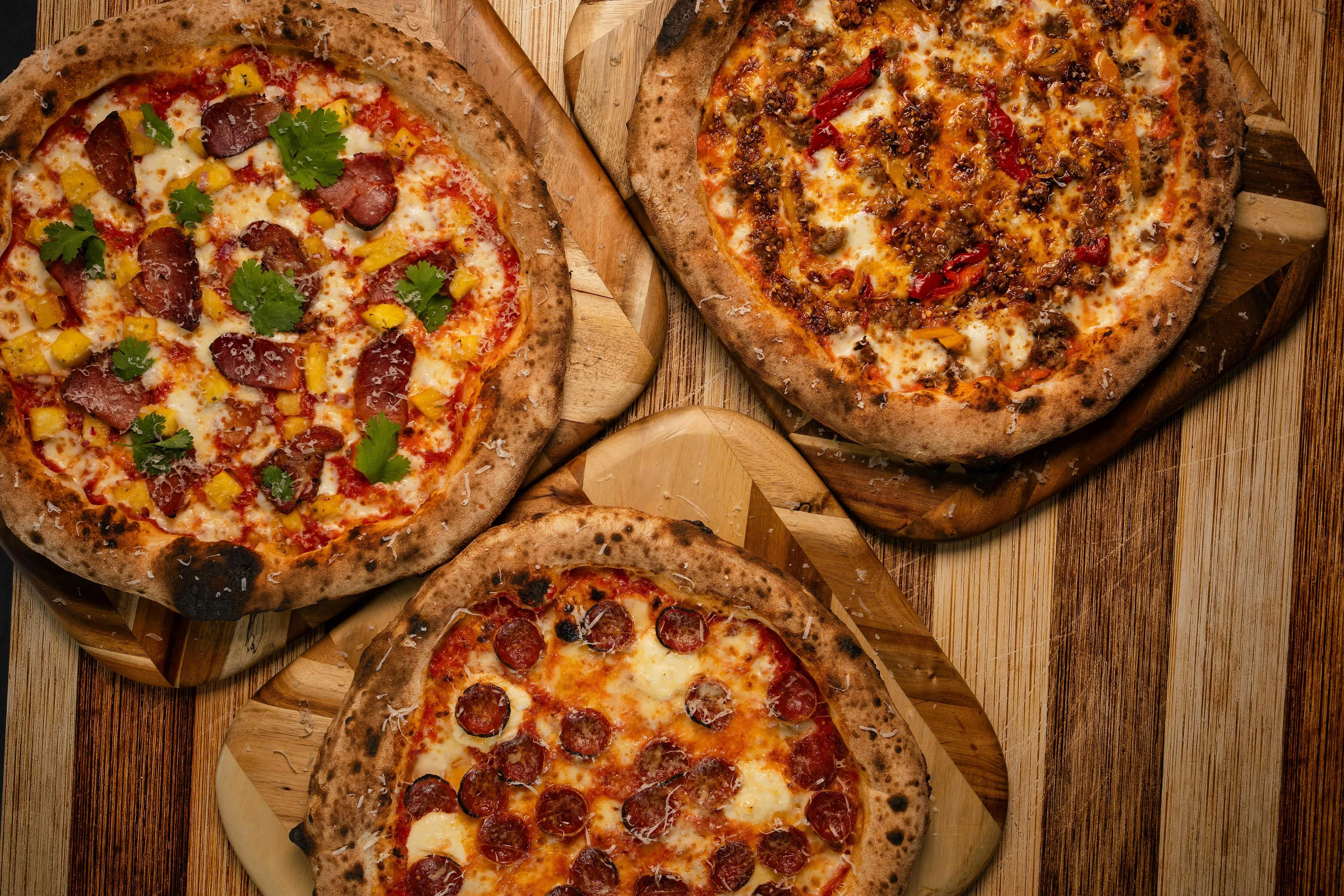 Three gourmet pizzas on wooden boards