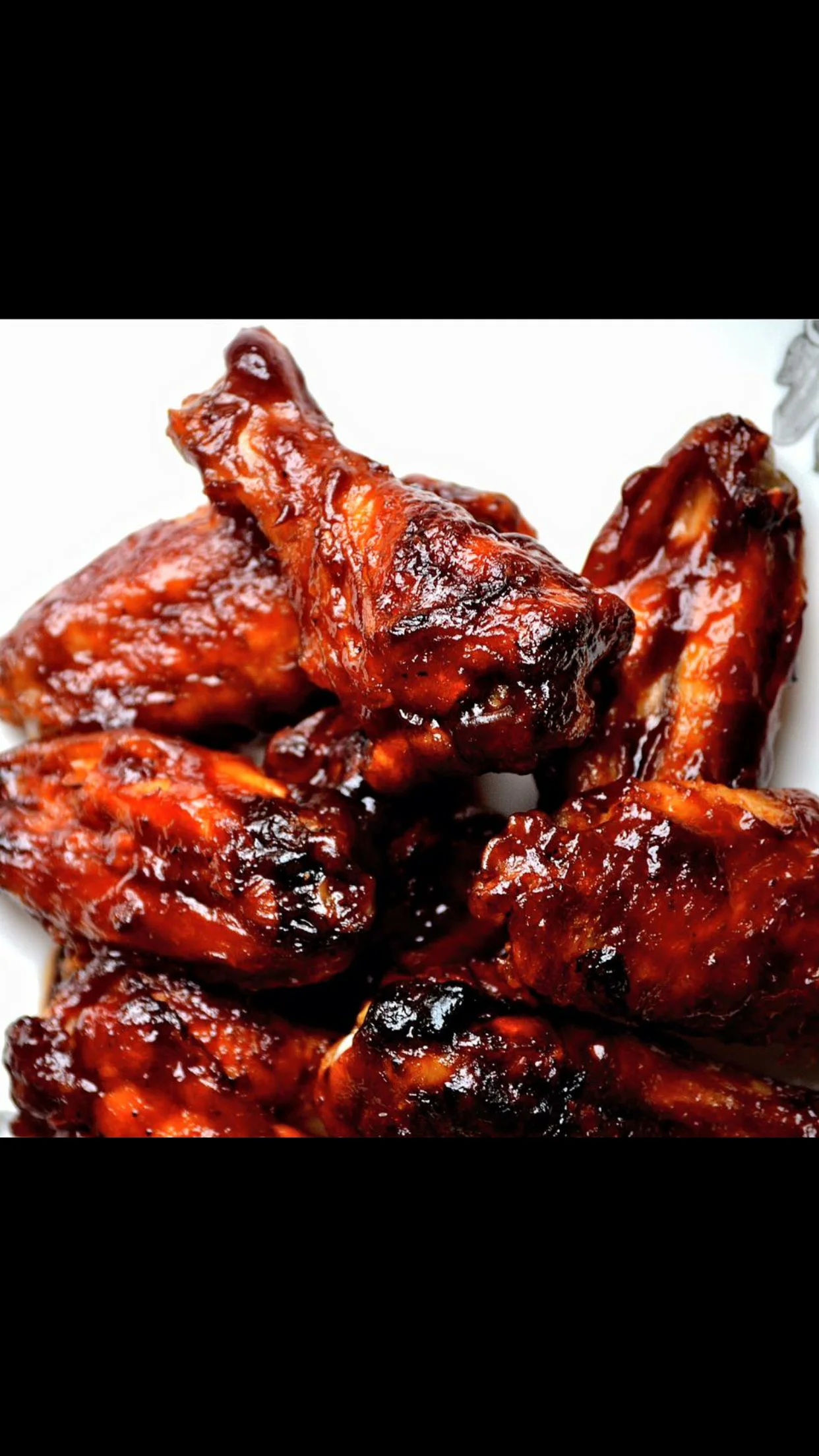 A plate of glossy barbecue chicken wings, shiny with sauce and garnished for a mouthwatering appearance.