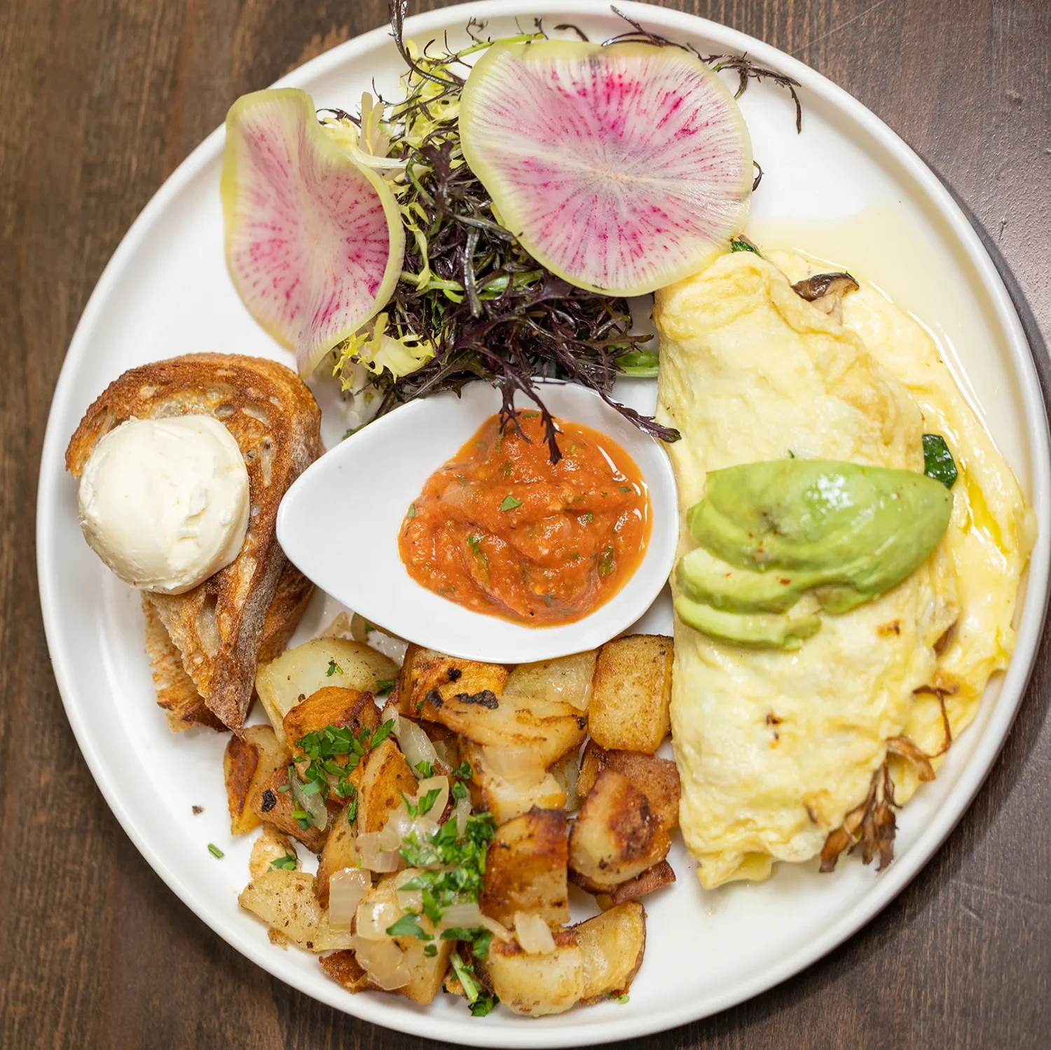 Plated avocado omelette served with roasted potatoes, artisan toast, fresh greens, and tomato salsa at Sprout Cafรฉ in Palo Alto