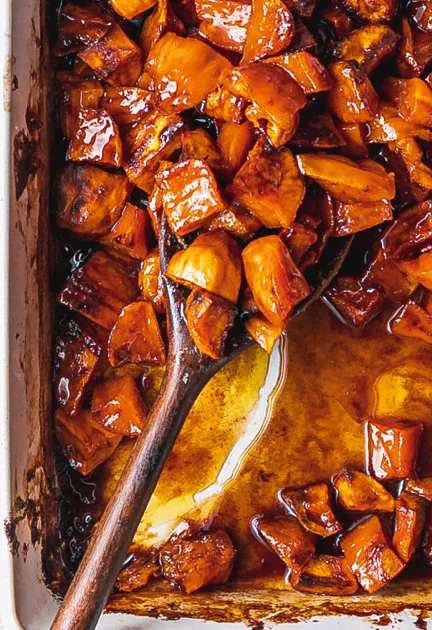 A close-up of caramelized diced fruit in a glossy sauce, presented in a dish with a wooden spoon resting inside.