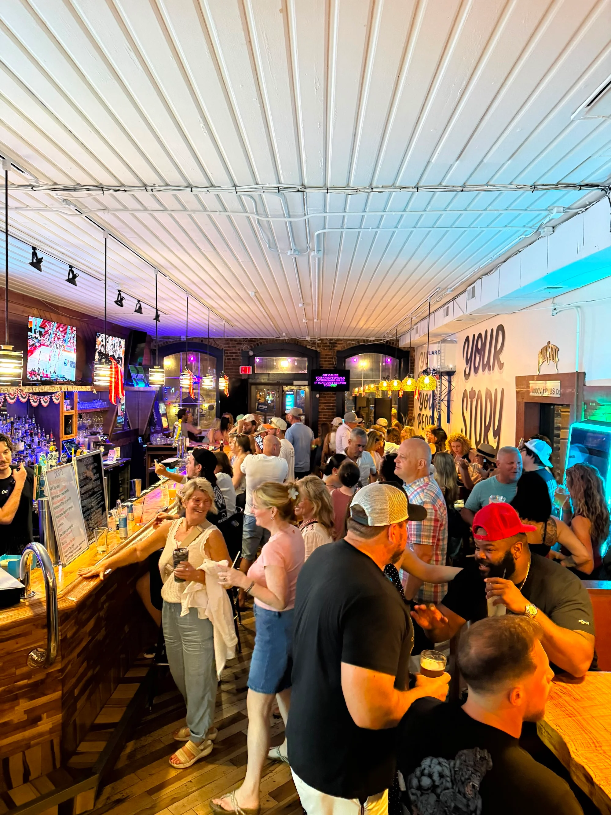 A crowded bar area filled with patrons, lively ambiance, and colorful lighting while people engage in conversation.