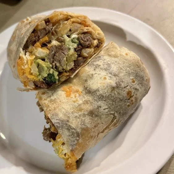 A cross-section of a burrito filled with beef, cheese, and vegetables, wrapped in a crispy tortilla. It is served on a white plate.