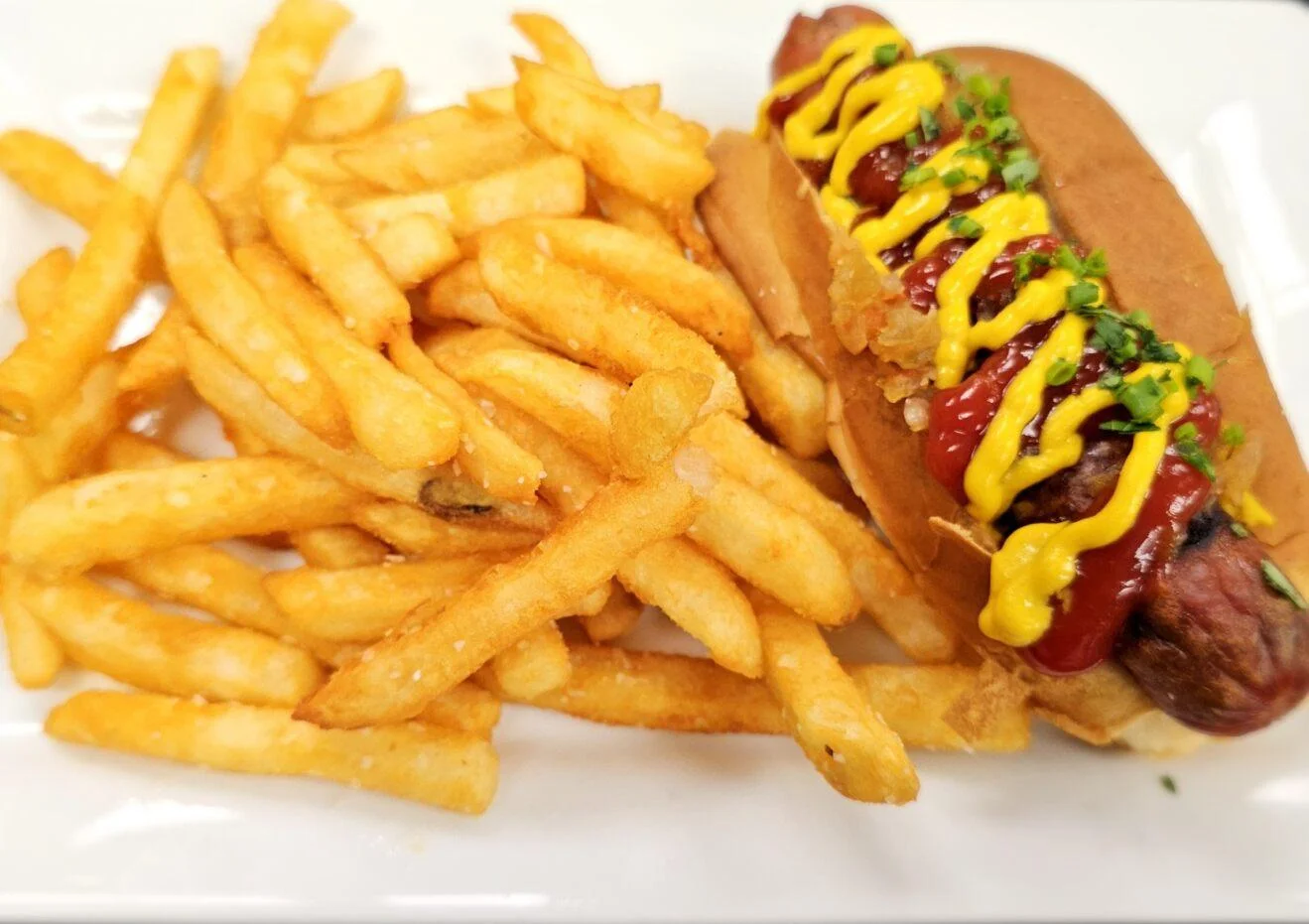A hot dog topped with mustard, ketchup, and crispy onions, served alongside a generous portion of golden French fries on a white plate.